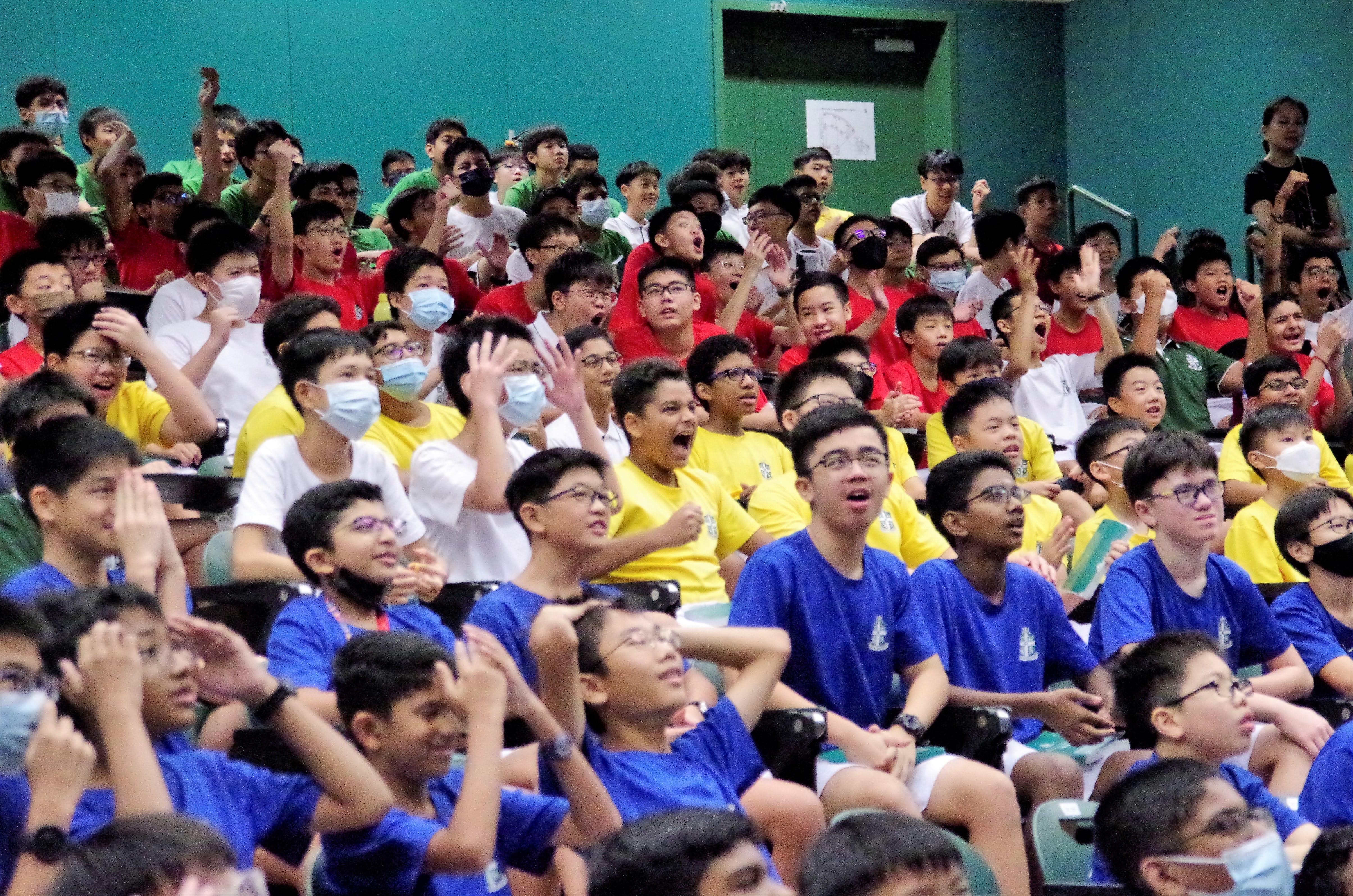 A large crowd of students in colored house t-shirts cheering and raising their hands in an auditorium.